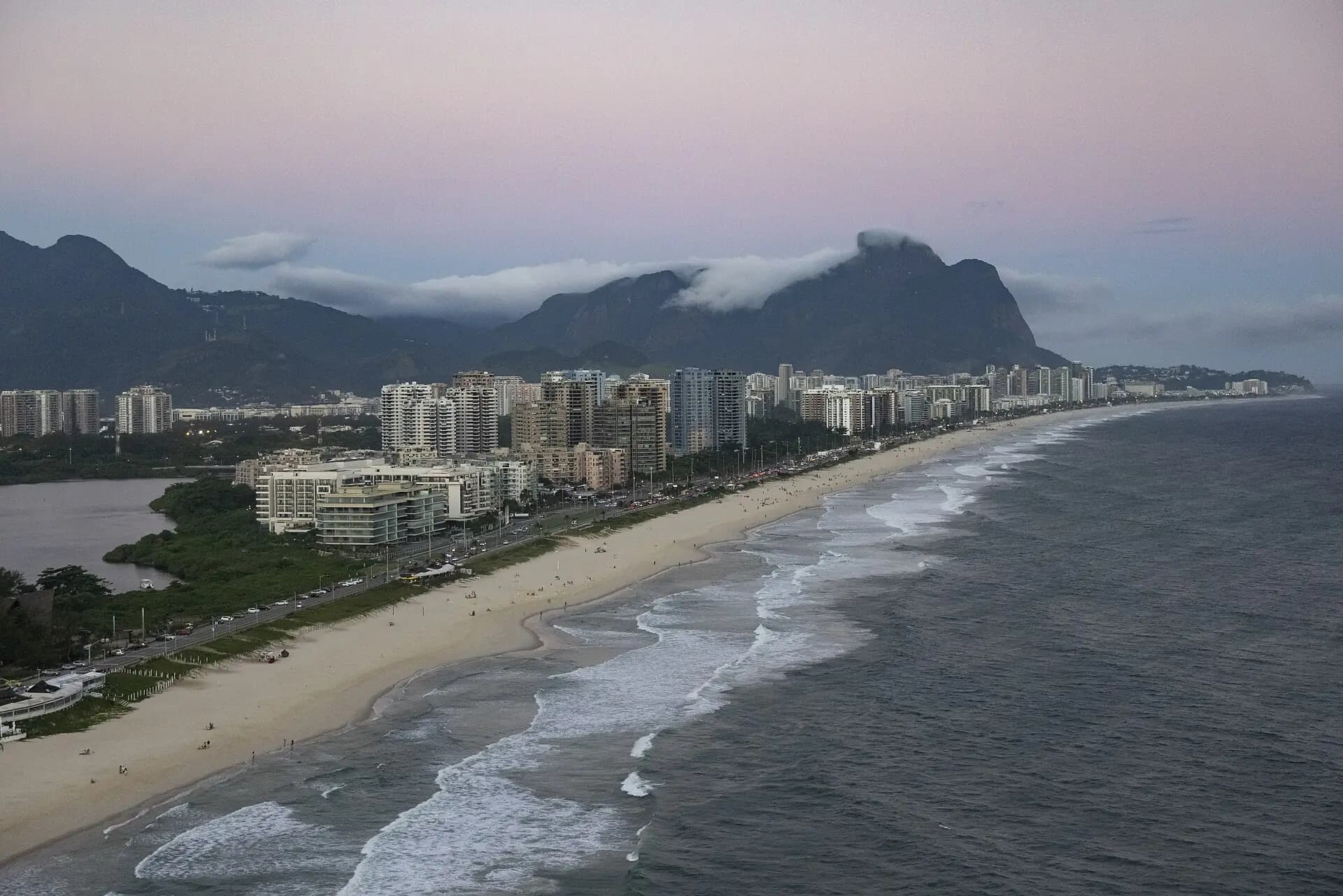 Praia da Barra da Tijuca ao entardecer, com os prédios da orla e a Pedra da Gávea